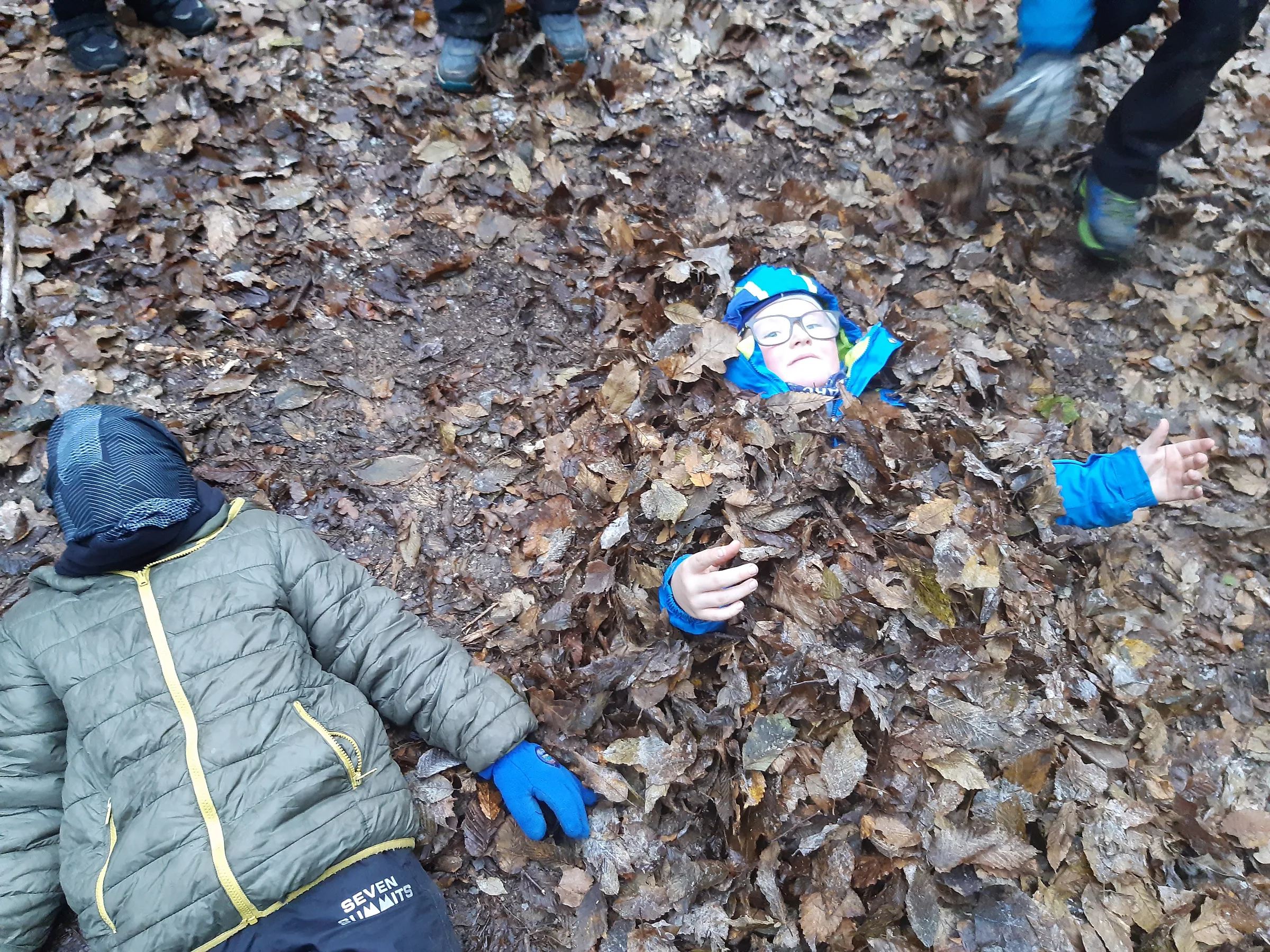Ein Kind hat sich im Herbstlaub vergraben, nur das Gesicht schaut heraus