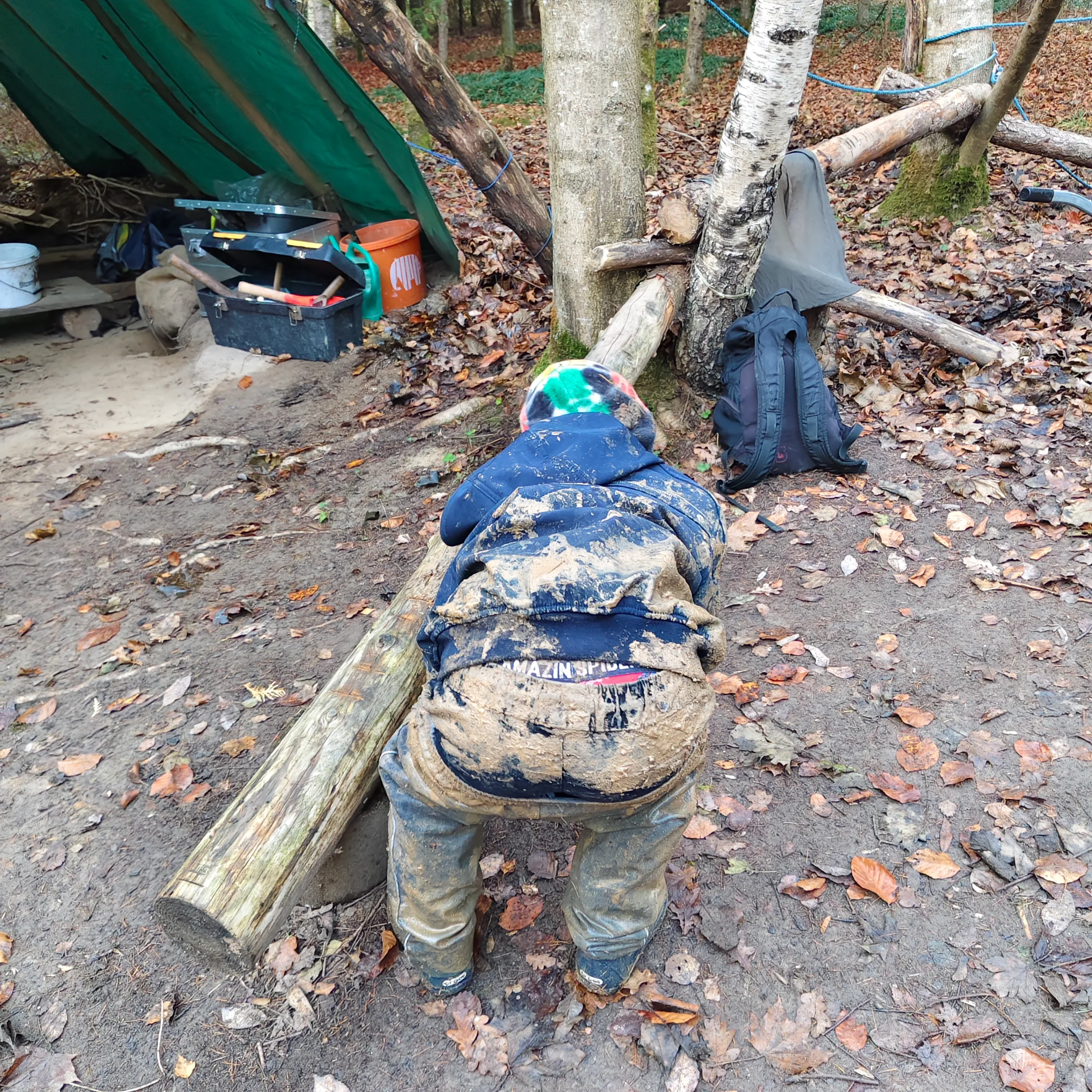 Ein Kind schiebt einen Baumstamm über den Waldboden